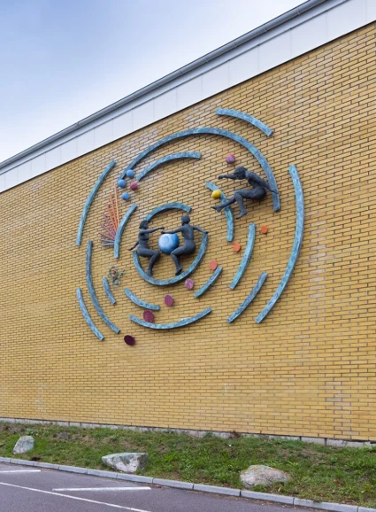 Väggkonstverk med koncentriska cirklar där tre människor, bollar och stavar verkar röra sig.