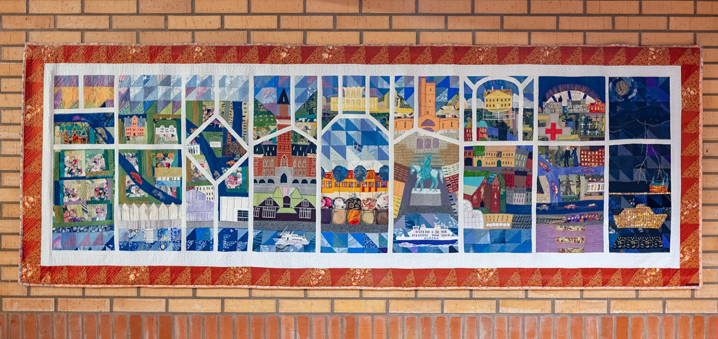 Rektangulär textiltavla uppdelad i fält med olika motiv i.