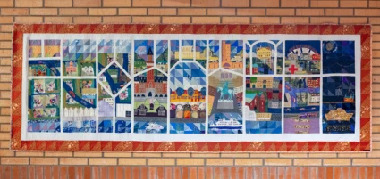 Rektangulär textiltavla uppdelad i fält med olika motiv i.