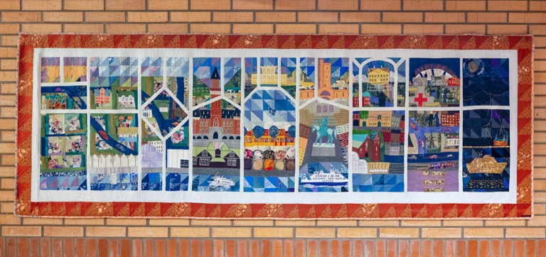 Rektangulär textiltavla uppdelad i fält med olika motiv i.