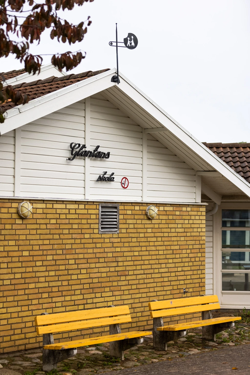 Utomhusmiljö med gavel, vimpel och bänkar framför.