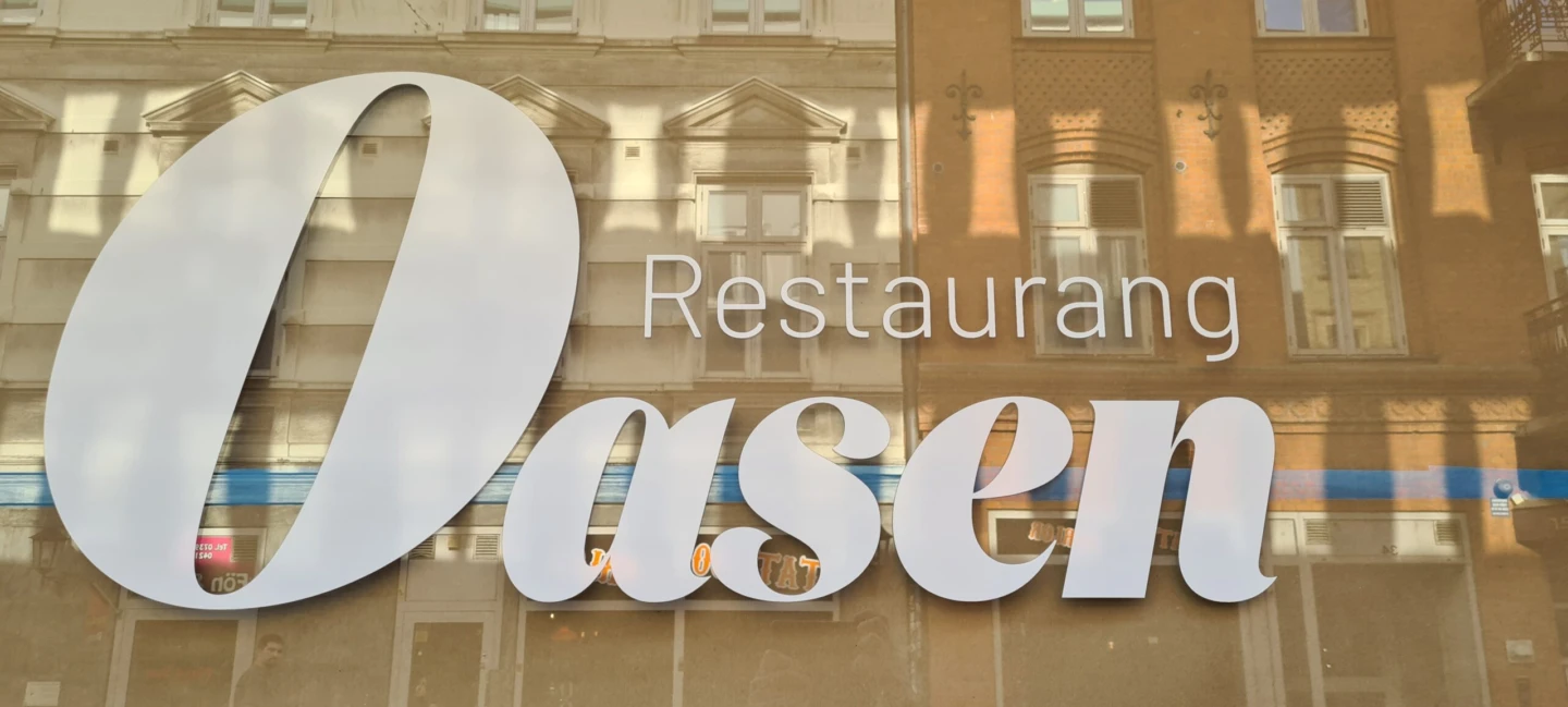 Fönster med Oasens namn på i vit fönsterfolie.