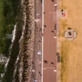 En drönarbild. Vi ser en löparbana och en solbränd gräsmatta under oss. Människorna där nere är små som myror.
