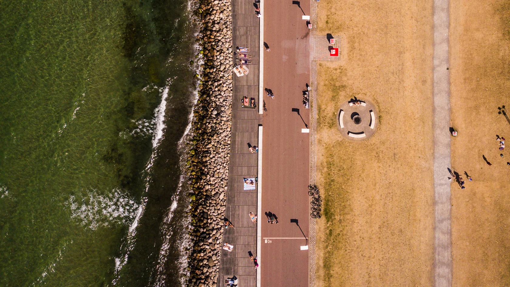 En drönarbild. Vi ser en löparbana och en solbränd gräsmatta under oss. Människorna där nere är små som myror.