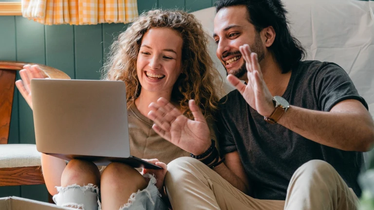 Två personer, kanske är de ett par, sitter vid en laptop och ser glatt koncentrerade ut.