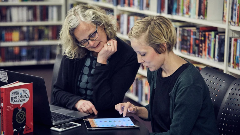 En medelålders person och en tonåring läser intresserat på en surfplatta tillsammans.