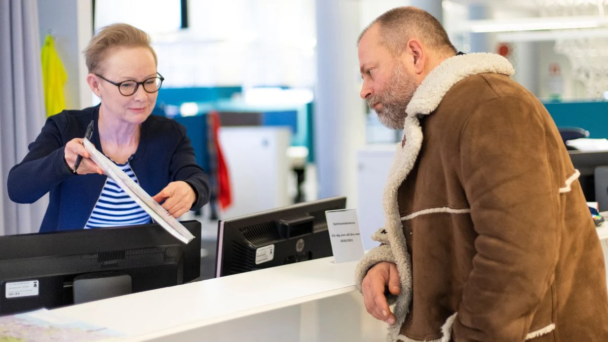 En kvinna visar ett papper för en man. Hon står bakom en infomrationsdisk.