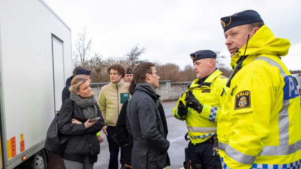 Två poliser i gula reflexvästar står intill en mindre grupp människor.