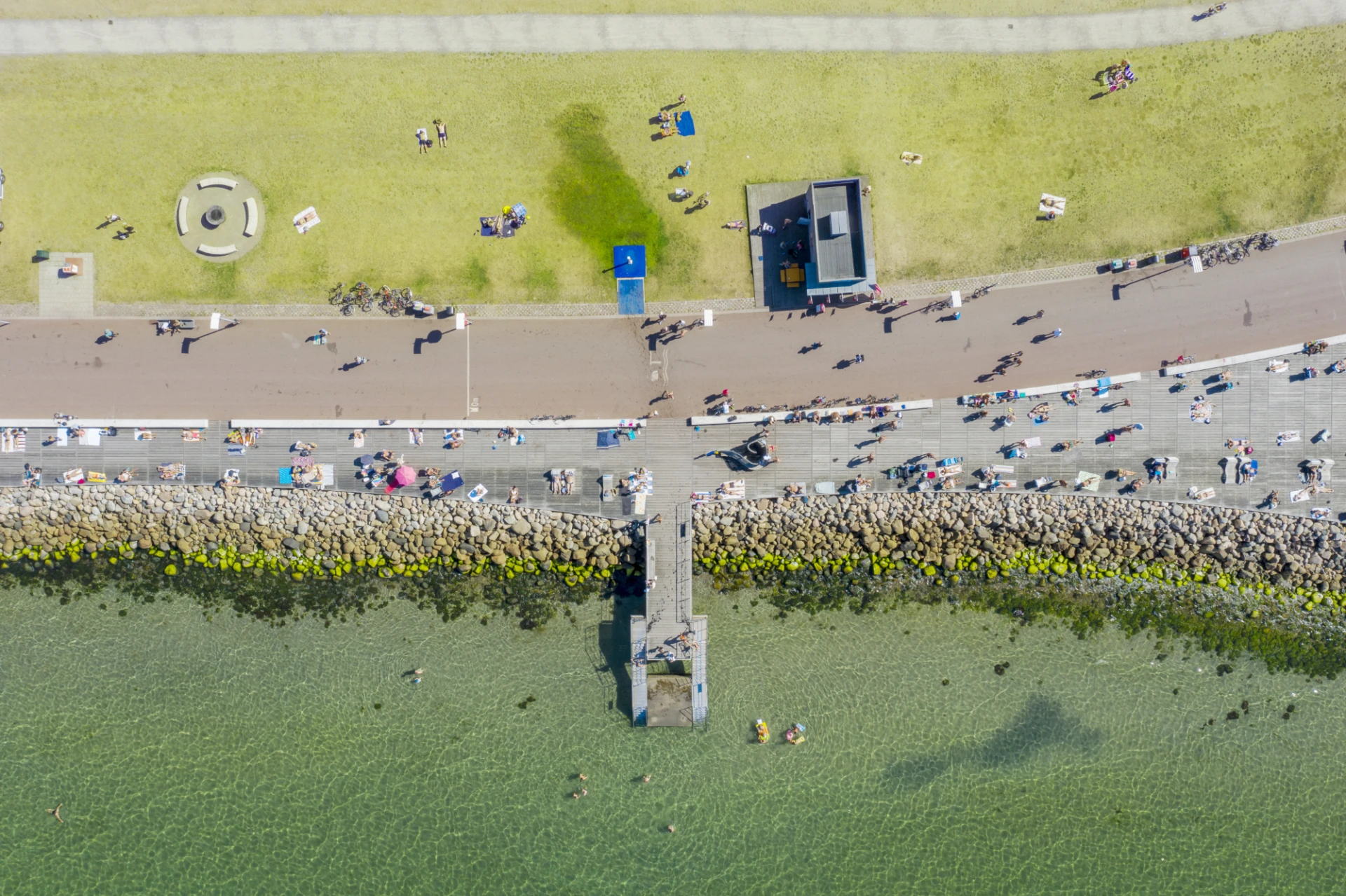 En del av Gröningen fotograferad rakt ovanifrån, med brygga, strandpromenad och människor som njuter av sommaren.