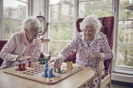 Två äldre kvinnor sitter vid et bord och spelar fia med knuff.