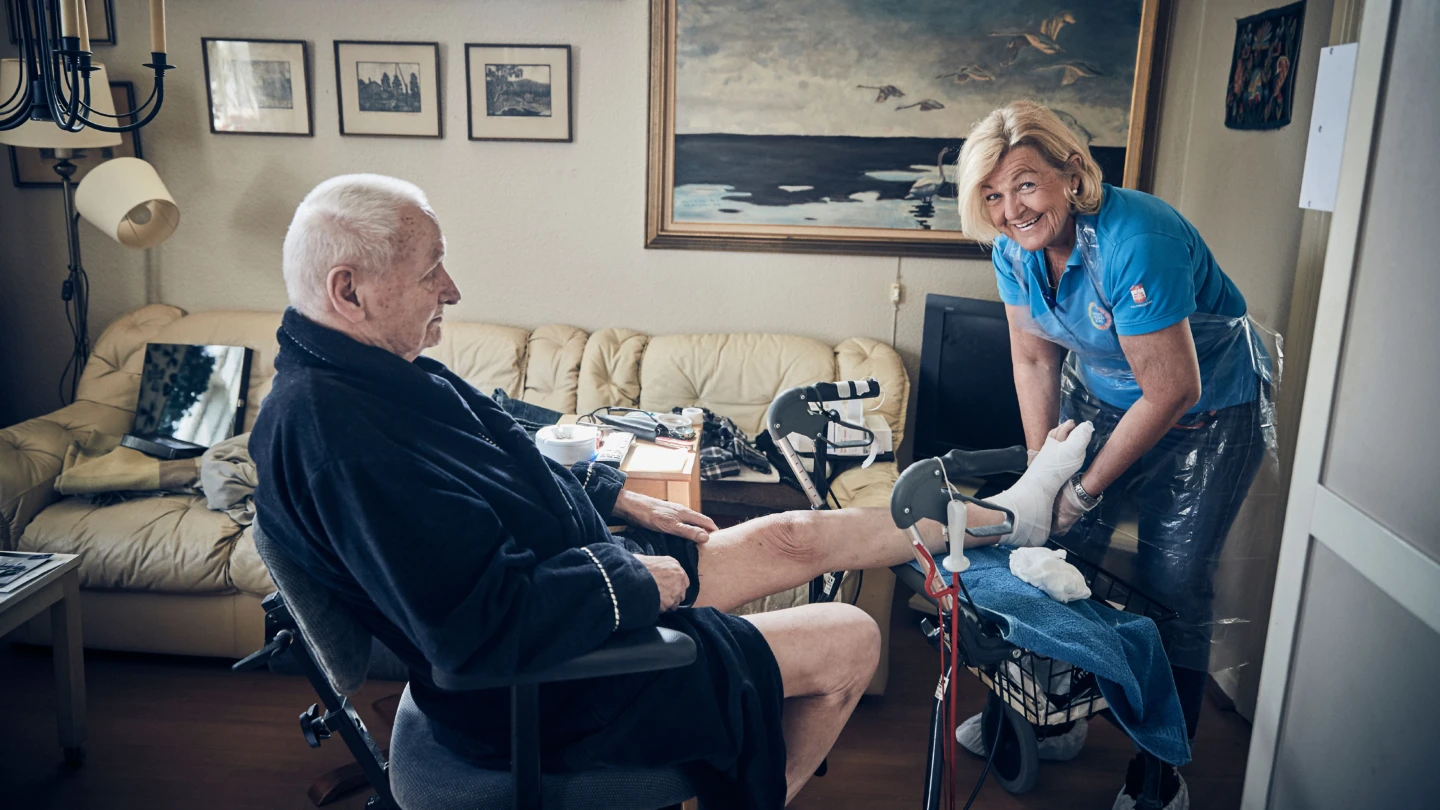 man som sitter ned på en stol, kvinna i arbetskläder håller i hans fot och ler