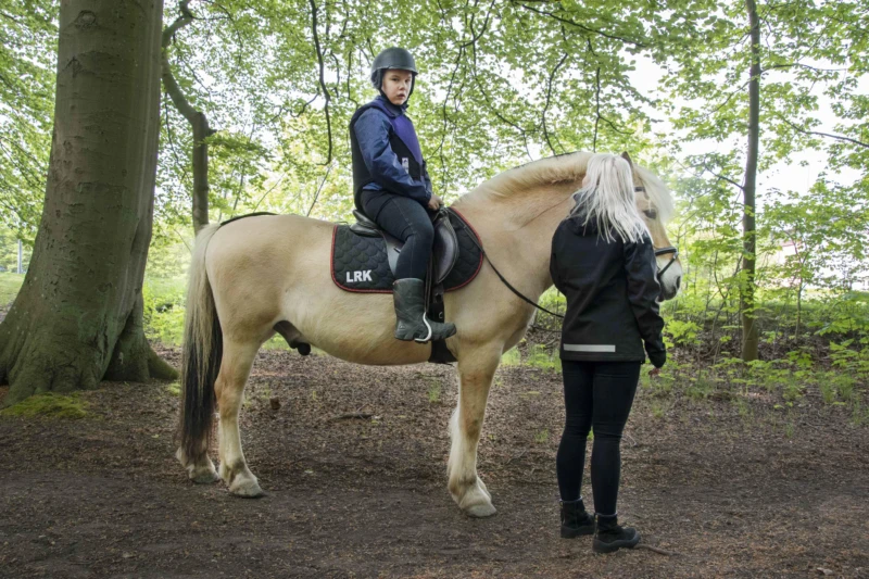 Emmy känner sig trygg på hästryggen och vill gärna att det ska gå undan. Stödassistent Johanna följer med henne för att se till så att allt går bra.