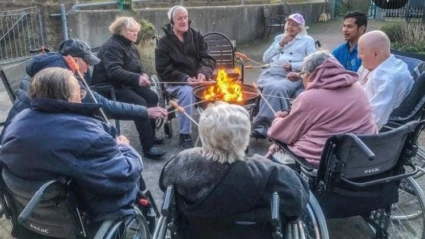 Ett gäng seniorer i rullstol sitter runt en öppen eld.
