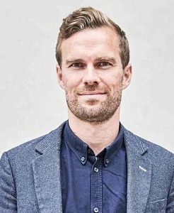 Man med kort hår, blå skjorta och grå kavaj