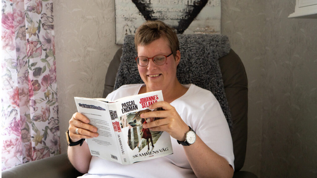 Kvinna med glasögon sitter i en fåtölj och läser en bok