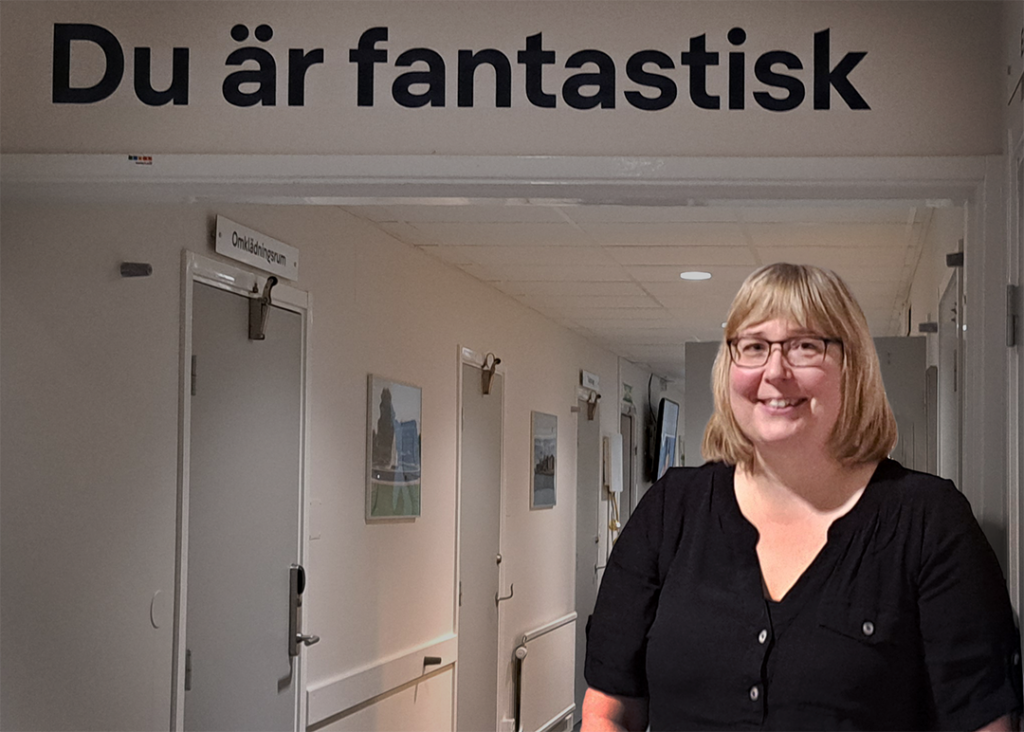 Kvinna i svart blus står i en korridor. Ovanför henne på väggen står texten Du är fantastisk. 