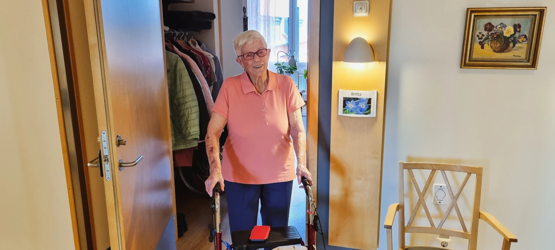 En äldre kvinna med rollator står i dörren till sin lägenheter