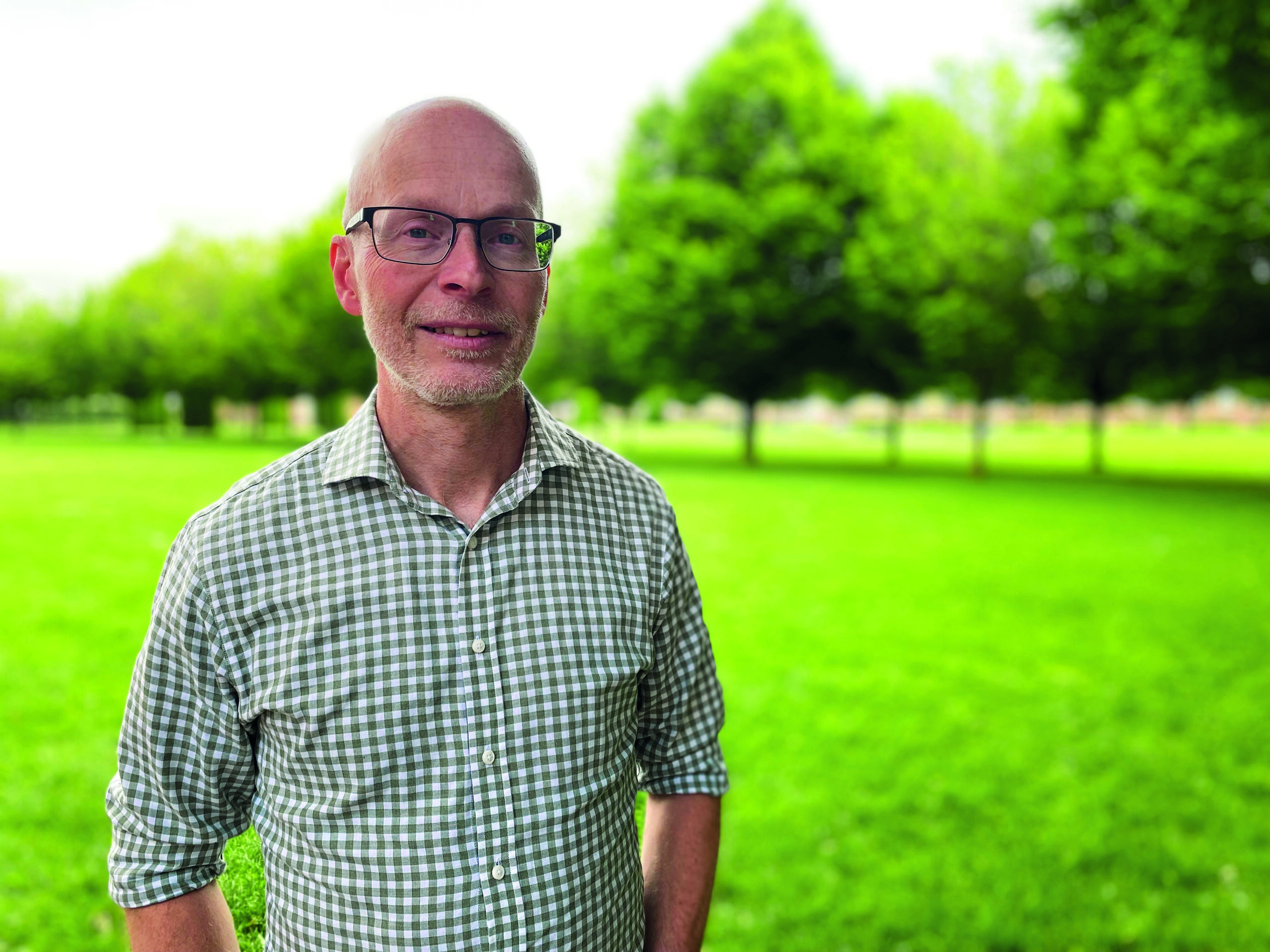 Man står på gräsmatta, tittar in i kameran och ler
