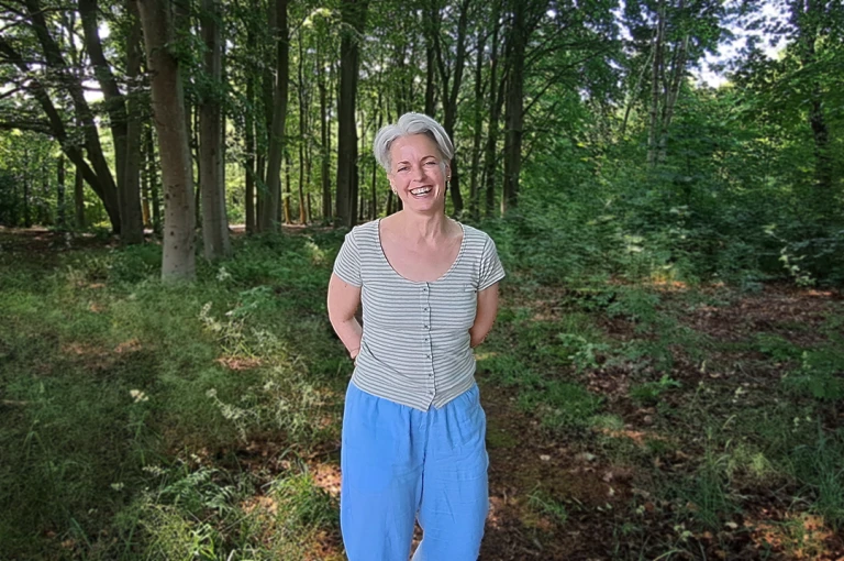 Kvinna i ljusgrön t-shirt och blå byxor står i skogen