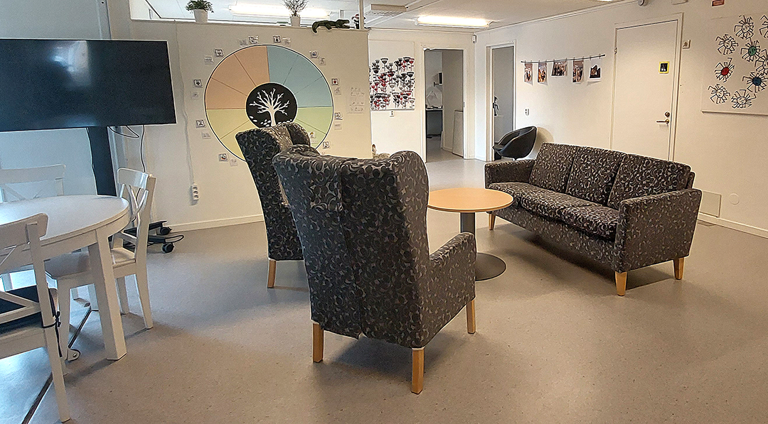 Rum med två fåtöljer och en soffa, en tv på rullstativ.