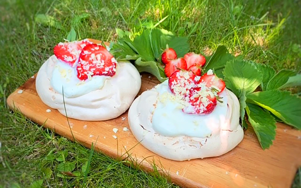 Två marängbakelser på en träbricka i gräset.