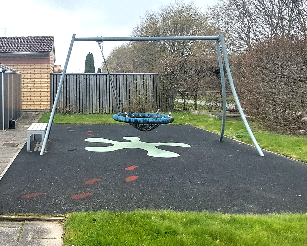 En gungställning utomhus på en svart yta med målad figur på. Gungan är en korggunga