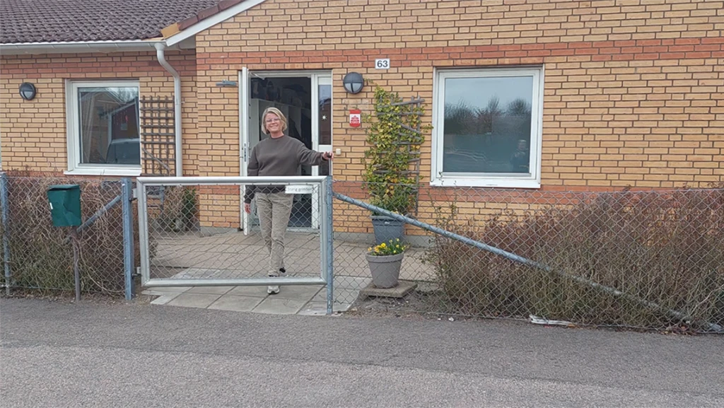 Gult tegelhus, en kvinna står vid grinden och öppnar den.