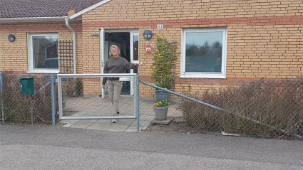 Gult tegelhus, en kvinna står vid grinden och öppnar den.