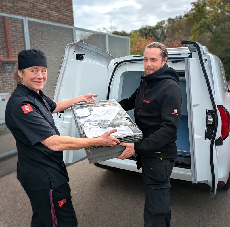 Medelålders kvinna lämnar över en låda full med mat till en yngre manlig chaufför.