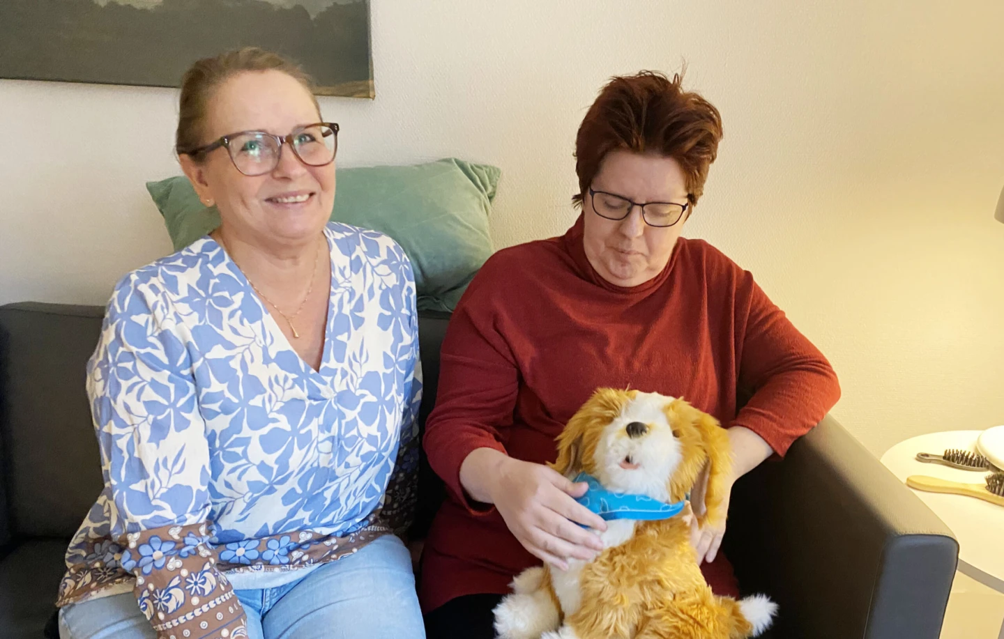 Två kvinnor sitter bredvid varandra i en soffa, den ena håller i en robot-katt