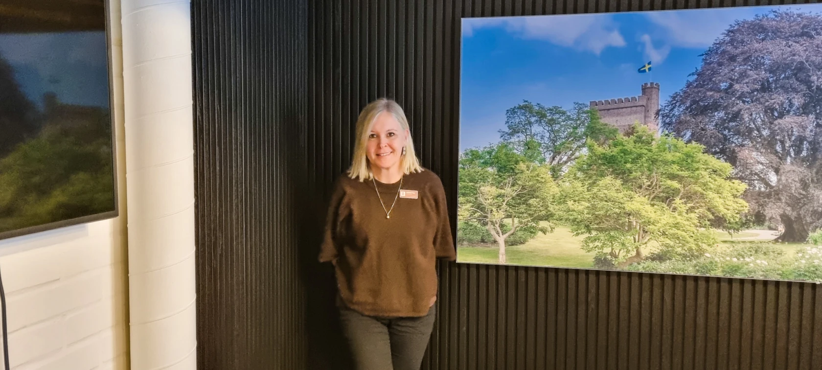 En kvinna står framför en mörk vägg, tittar in i kameran och ler.