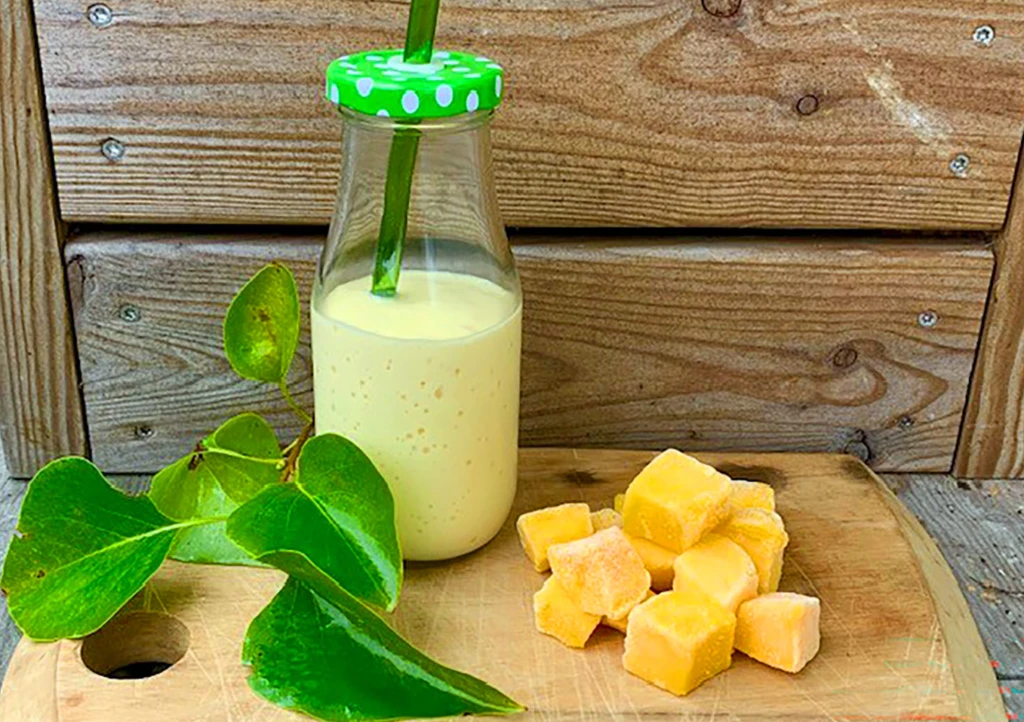 En glasflaska med smoothie och fryst mango på en bricka