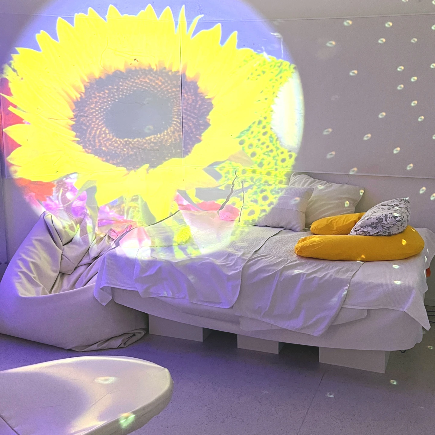 Ett mysigt vitt och ljust rum med en säng och ljusspel på väggarna.