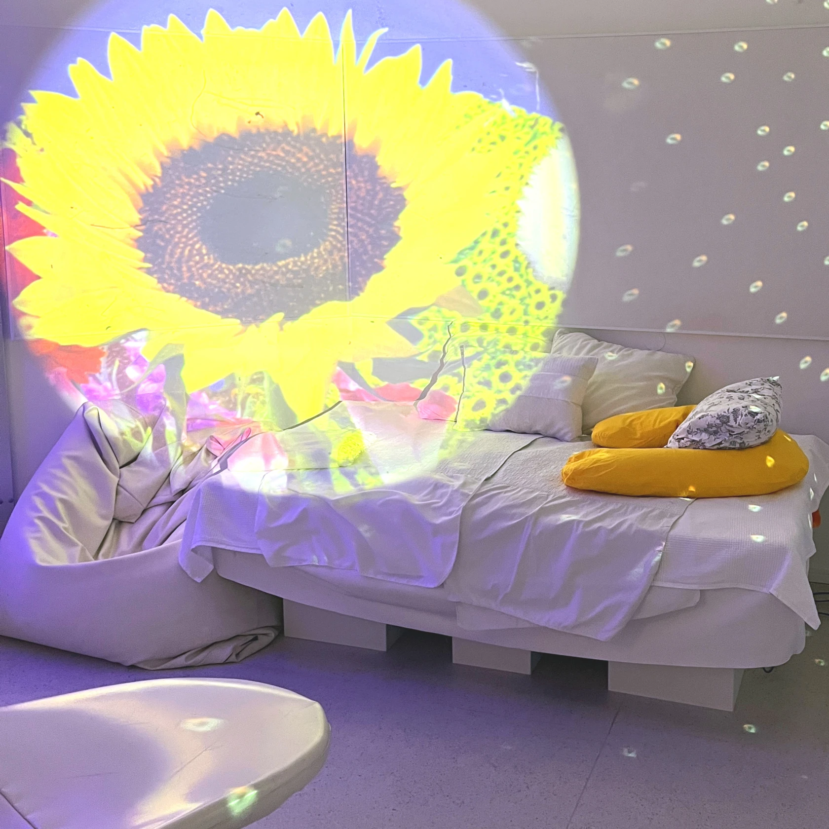 Ett mysigt vitt och ljust rum med en säng och ljusspel på väggarna.