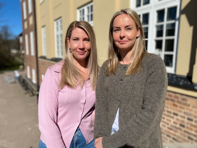 Två kvinnor står utanför ett hus i starkt solljus