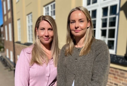 Två kvinnor står framför ett hus i starkt solljus