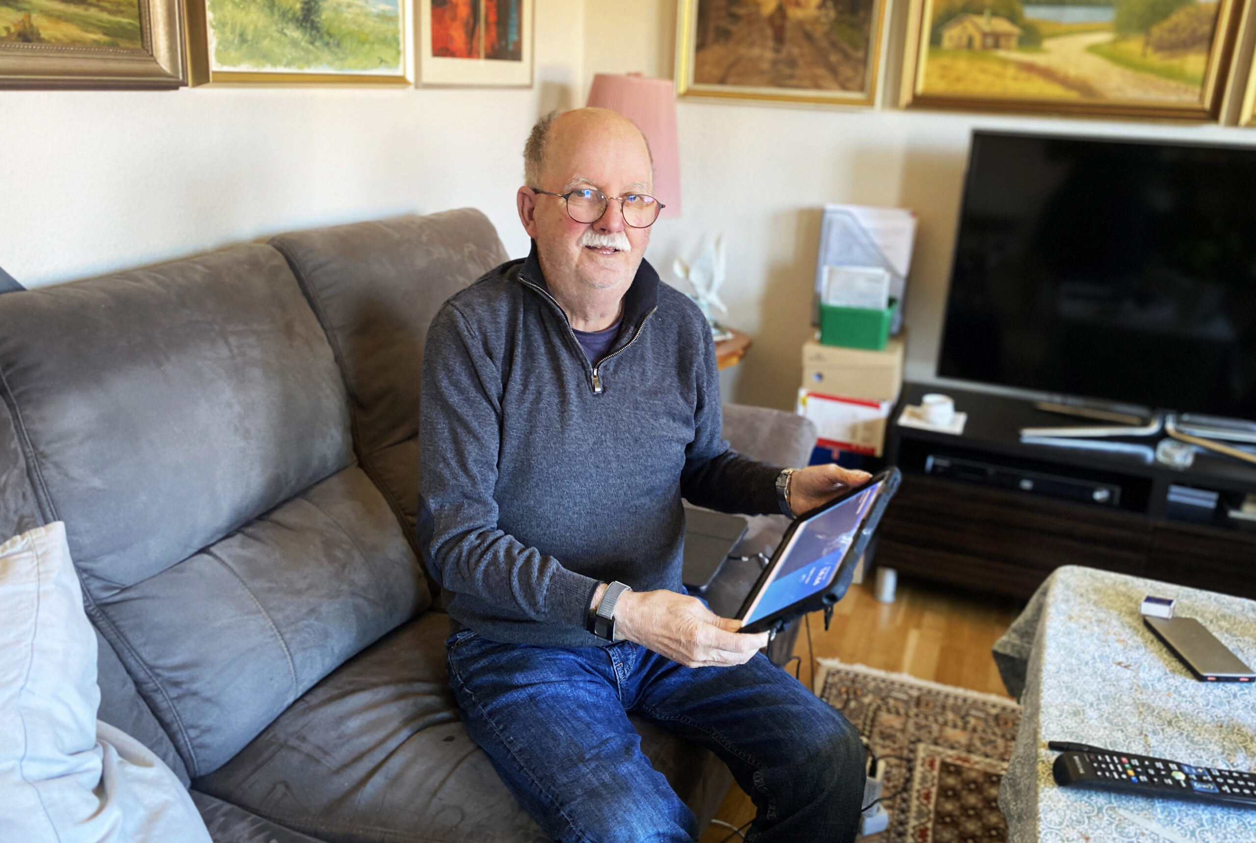 En man sitter i en soffa, tittar in i kameran och ler.