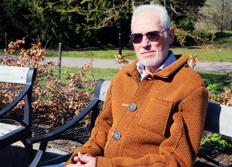 En äldre man sitter på en parkbänk i solskenet
