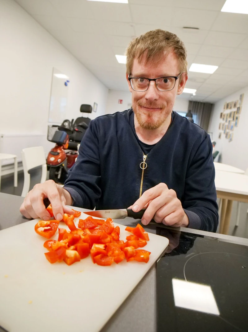 En person skär paprika och tittar in i kameran.