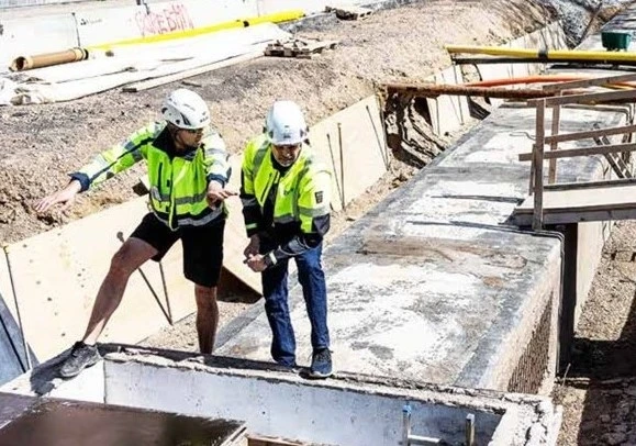 Två personer i byggarbetskläder står och gestikulerar vid en fjärrvärmeanläggning.