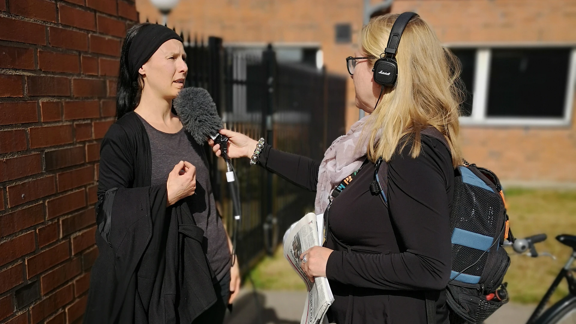 Sarah Perfekt blir intervjuad om fotoutställningen Håll avstånd på Furutorpsplatsen.