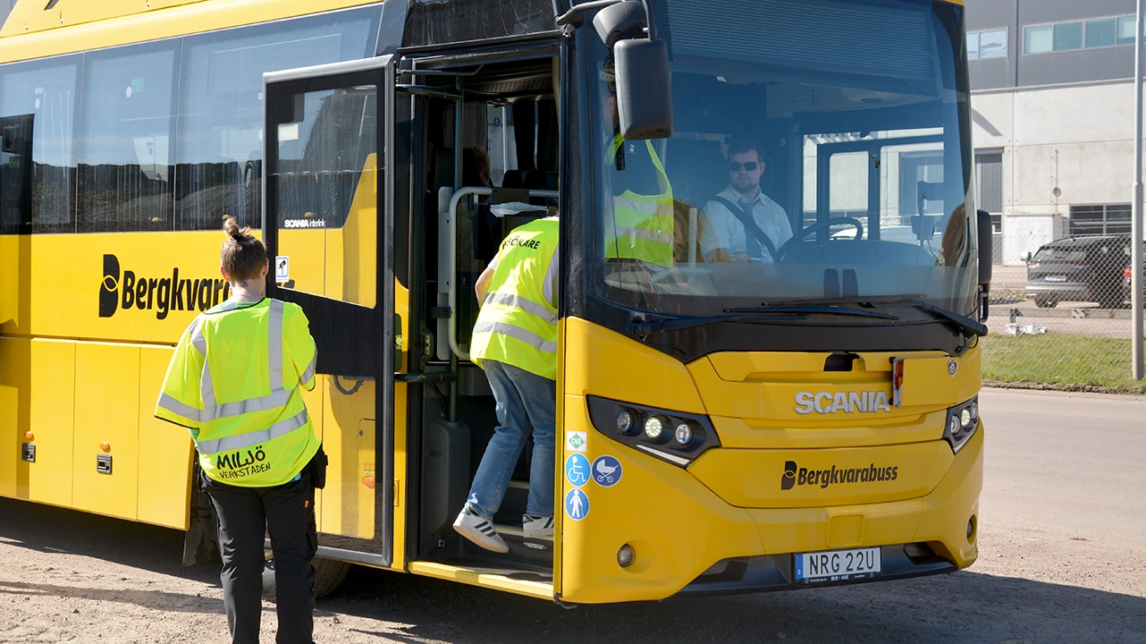 En pedagog från Miljöverkstaden och en elev går på en gul buss.