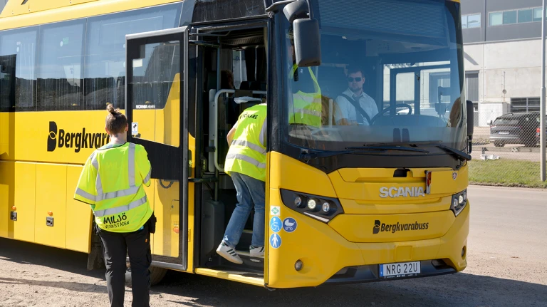 En pedagog från Miljöverkstaden och en elev går på en gul buss.