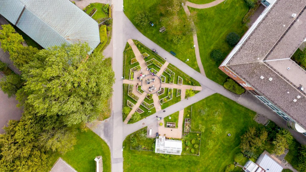 Ett grått växthustak i en grön park med gångar i trekant sett uppifrån himlen.