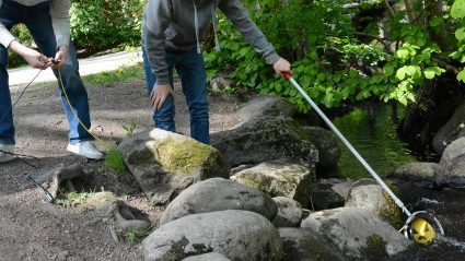 Två elever håller i en stav med ett gult hjul längst ut som snurrar i det strömmande vattnet.