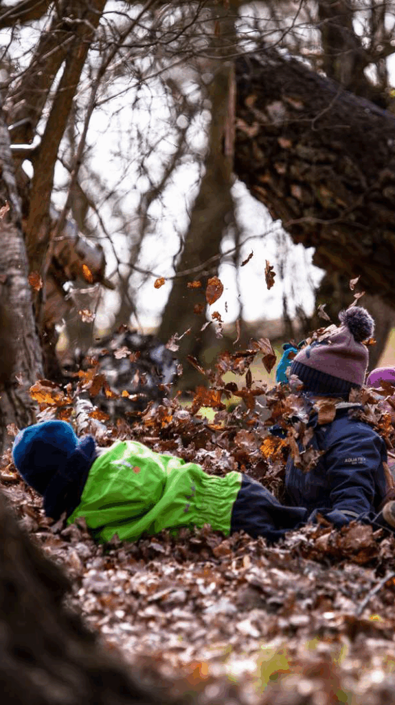 Två barn som rullar runt i löv, så att de nästan inte syns.