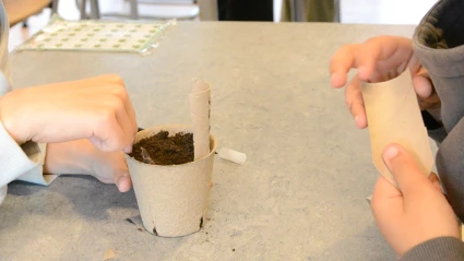 Två elever pillar med en pappmugg fylld med jord.