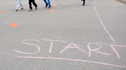 Barn som springer på en skolgård där texten "Start" är skriven med rosa krita.