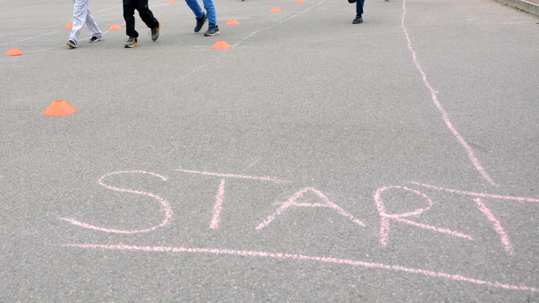 Barn som springer på en skolgård där texten "Start" är skriven med rosa krita.