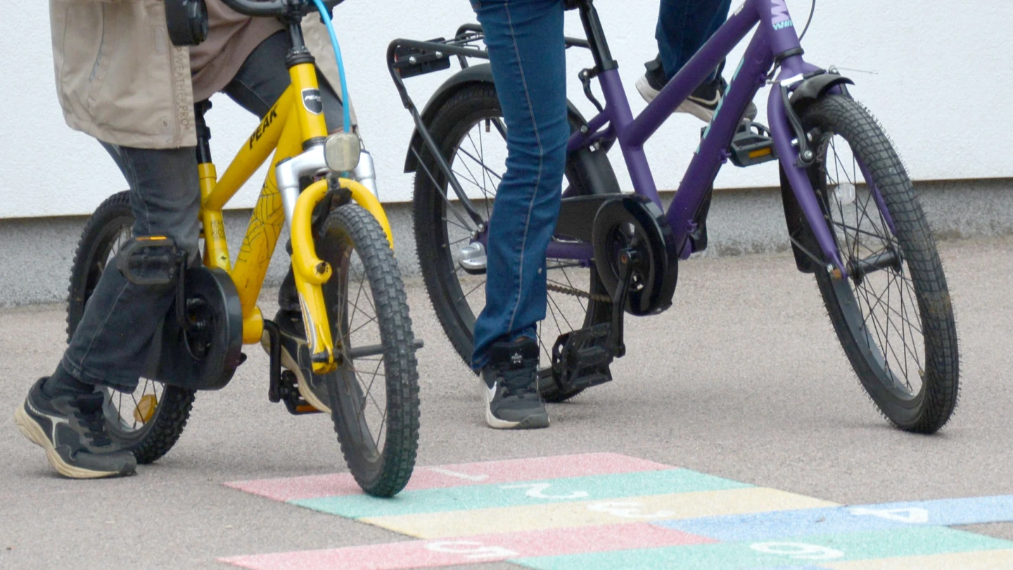 Två barn som cyklar på en skolgård med en färgglad hopphage.